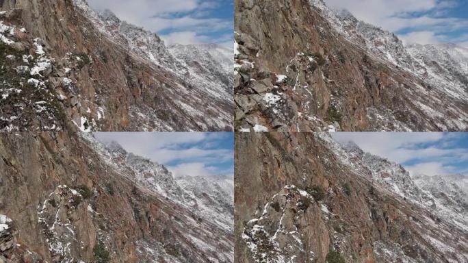 鸟瞰图相机的近距离跨度，在早春的山坡上，高高的岩壁旁，绿草如茵，雪如山