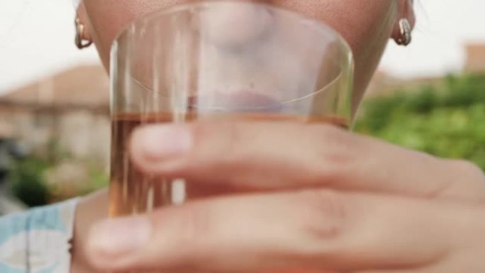 女人正在喝苹果或葡萄汁。女性的手将装有苹果或葡萄汁的玻璃杯带到嘴里，并在大自然的晴天喝。特写