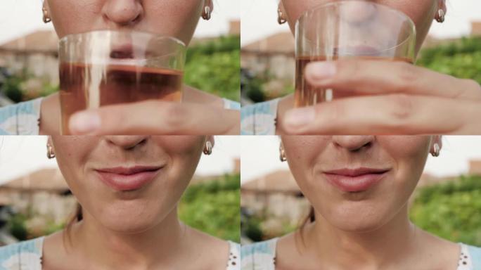 女人正在喝苹果或葡萄汁。女性的手将装有苹果或葡萄汁的玻璃杯带到嘴里，并在大自然的晴天喝。特写
