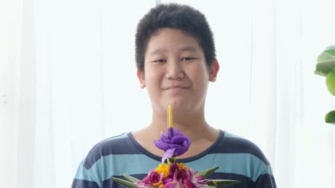 快乐的亚洲男孩在家中拿着克拉通 (用香蕉叶和花朵制成，漂浮在河中祈祷和感谢)，为夜间做准备。