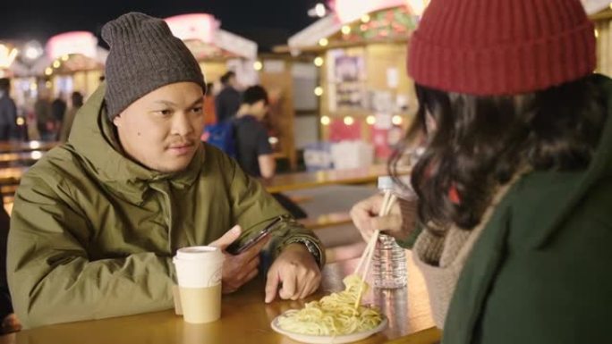 亚洲夫妇穿着暖和的衣服在圣诞节吃街头食物。