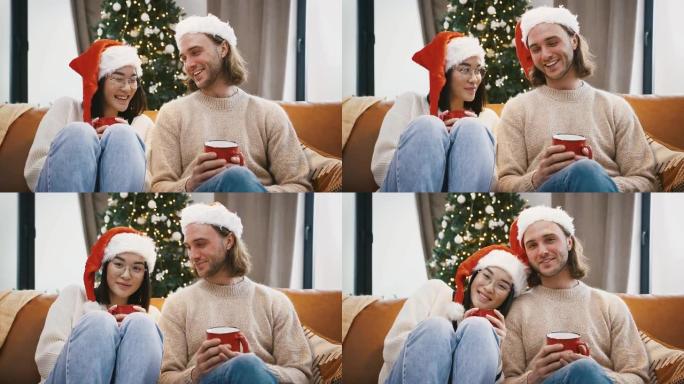 多种族的男性和女性笑着，说话，拿着一杯茶，坐在沙发上，靠着装饰好的圣诞树