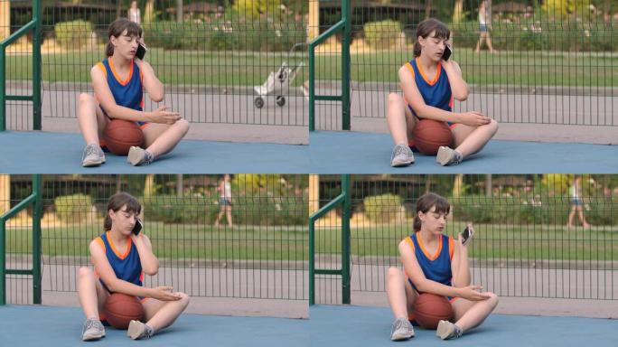 一名女运动员坐在篮球场上，带球，输入消息，然后在智能手机上聊天。特写。慢动作