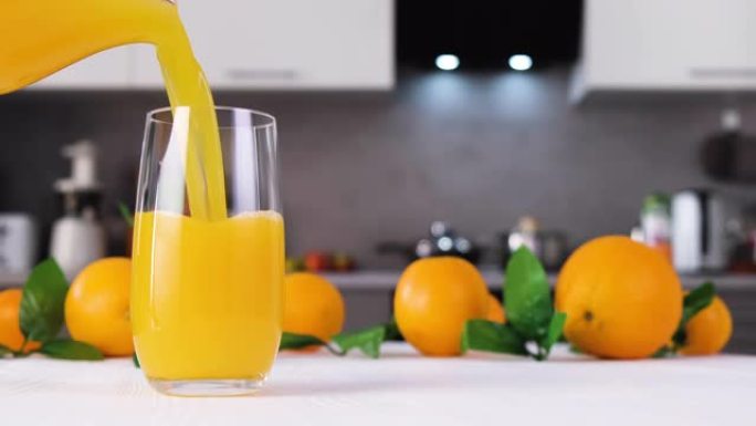 橙汁倒入白色桌子上的玻璃杯中。柑橘汁飞溅慢动作