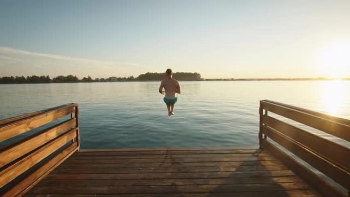 一个年轻人跑下码头，像炸弹一样跳进湖里。在湖上休息。日落。4 k