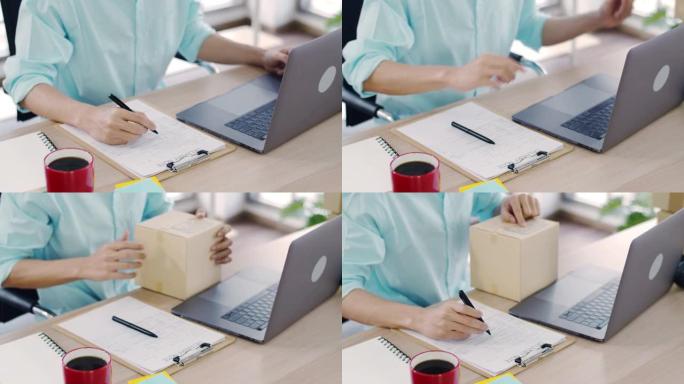 在新型冠状病毒肺炎大流行期间，亚洲人小企业主在家庭办公室使用笔记本电脑和托运包装箱。