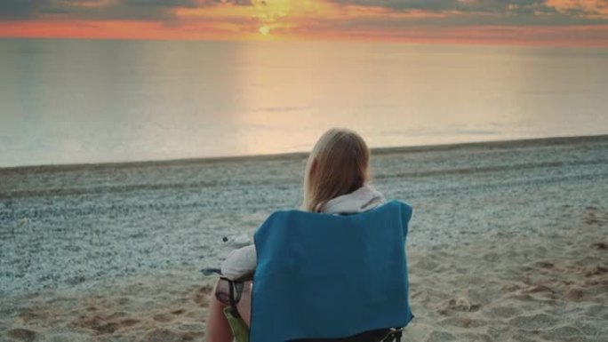 女人从保温杯中喝酒，日出前坐在沙滩上