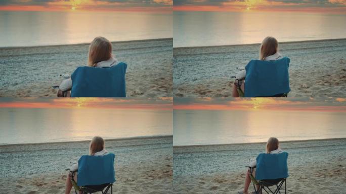 女人从保温杯中喝酒，日出前坐在沙滩上