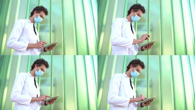年轻的男性医生在新型冠状病毒肺炎爆发期间使用平板电脑对抗绿墙时戴着医用口罩。高质量4k镜头
