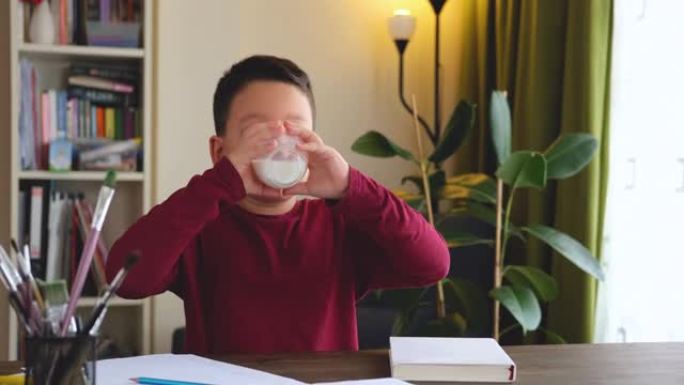 6-7岁可爱的孩子在桌子上喝牛奶。他知道他需要喝牛奶才能健康骨骼。他喜欢牛奶。