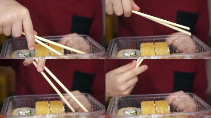 一个孩子手握筷子的特写镜头。孩子用筷子吃寿司。在食物容器中开胃寿司。全球食品配送。选择性聚焦，浅景深