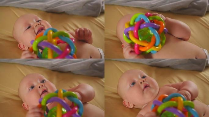 微笑的婴儿躺在床单上的床上，用手握着玩具。儿童的感觉发育。特写镜头。