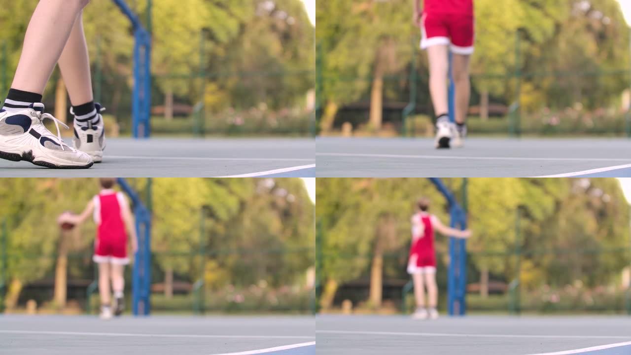 篮球位于运动场上。女运动员捡起球，运球到篮筐。独自练习街球。背景模糊。腿靠近。慢动作