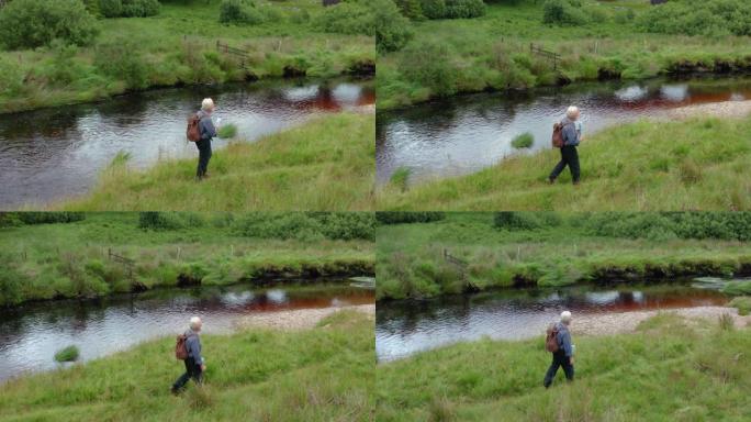 夏季，苏格兰西南部乡村一条小河边的一名活跃的高级男子的无人机的侧视图