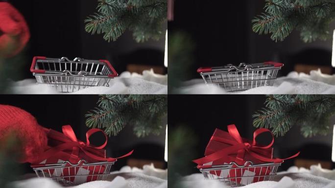 在树下的一堆雪上，一只手放在手套里放了一个购物篮，一个装有礼物的红色盒子被扔进去