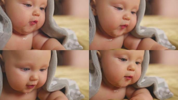 一个四个月大的胖乎乎的婴儿的肖像覆盖着灰色的毯子躺在肚子上。特写镜头。