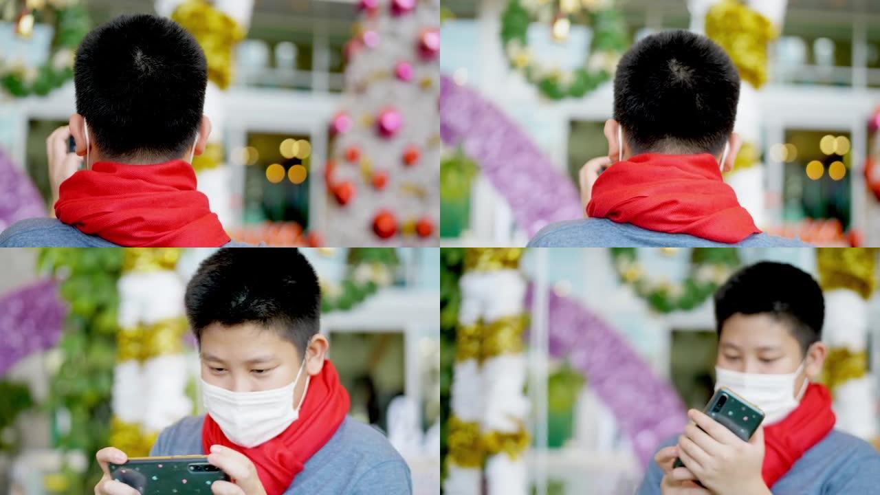 快乐的亚洲男孩戴着口罩和红领巾拍照或自拍自己的圣诞树装饰，节日概念。