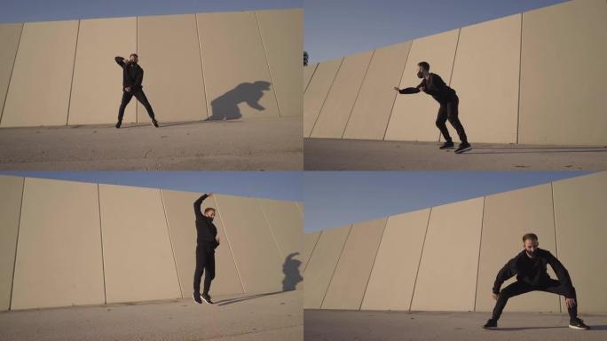 运动的年轻人穿着黑色的当代舞蹈，在灰色的墙壁前，做侧手轮，同时在城市户外练习杂技练习。