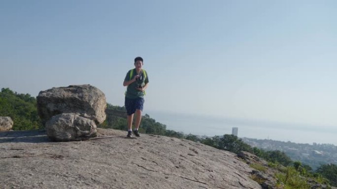 亚洲旅游男孩在山顶上奔跑，阳光明媚，户外冒险概念。