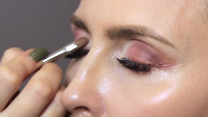 美容师将眼线涂在女孩眼睛的下眼皮上。专业化妆师用柔软薄眼妆刷特写视频