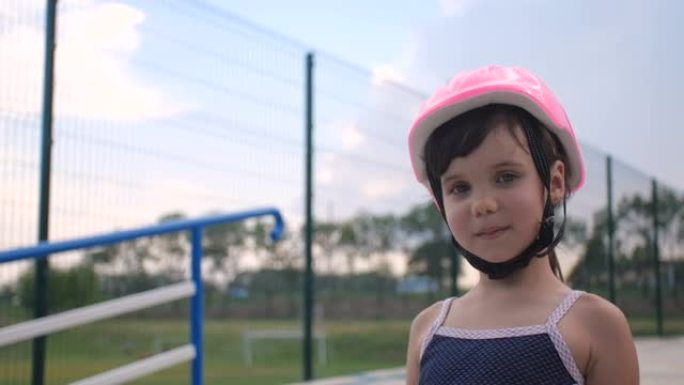一个小女孩第一次来到轮滑公园学习轮滑。一个戴着粉色安全帽的学龄前漂亮孩子的特写肖像，4k慢动作50 