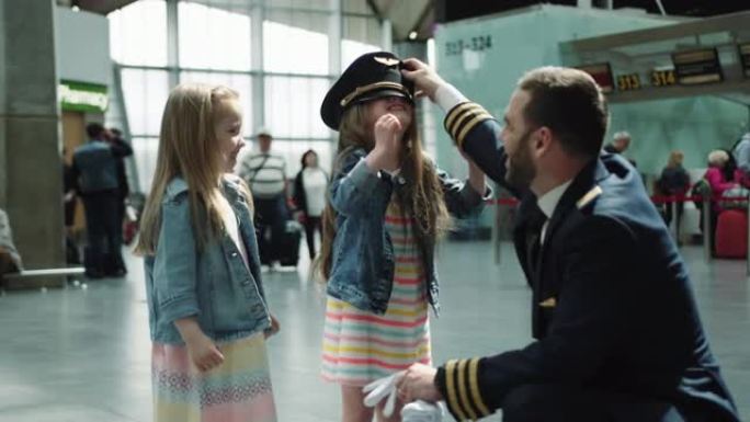 快乐的littke女孩试图在机场航站楼戴上dadies飞行员帽，看上去既开心又笑。在红色相机上拍摄的