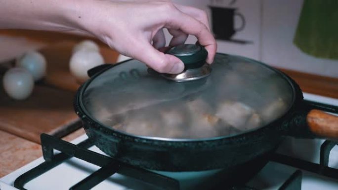 女性手打开盖子，在煎锅中检查准备就绪的肉。家庭厨房