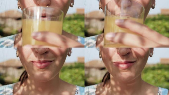 女人正在喝橙汁。女性的手将装有橙汁的玻璃杯带到嘴里，并在大自然的晴天喝。特写