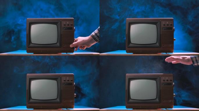 男人试图打开旧电视，敲它，散射灰尘颗粒。老式电视在带有蓝色霓虹灯的烟熏演播室背景下。男性双手靠近。慢