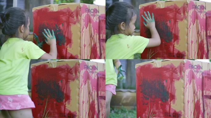 一位亚裔少女正在用手在纸盒上画颜色，孩子的抽象艺术学习活动