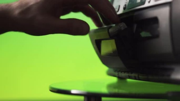 一名男子将录音带插入绿色背景的录音机中。手靠近。复古技术。上一代音频系统