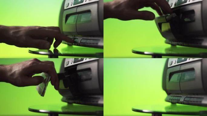一名男子将录音带插入绿色背景的录音机中。手靠近。复古技术。上一代音频系统