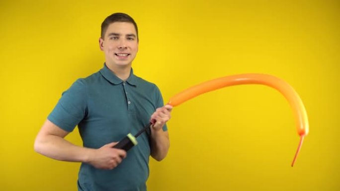 一个年轻人用黄色背景上的泵给一个长长的橙色气球充气。穿着绿色马球的男人。