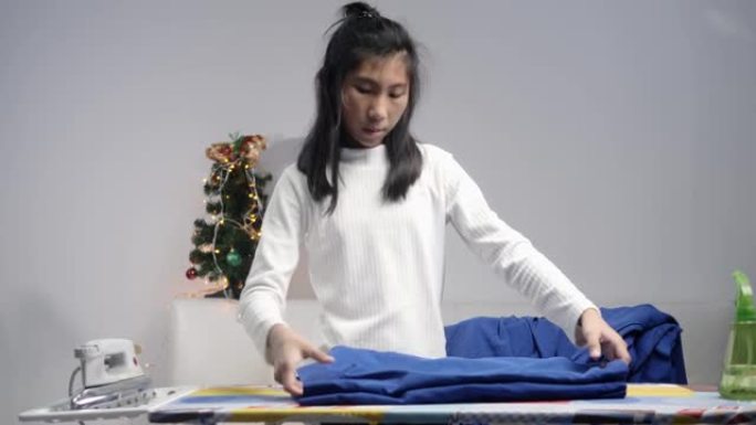 亚洲女学生熨烫她的校服，圣诞树装饰装饰背景，生活方式概念。