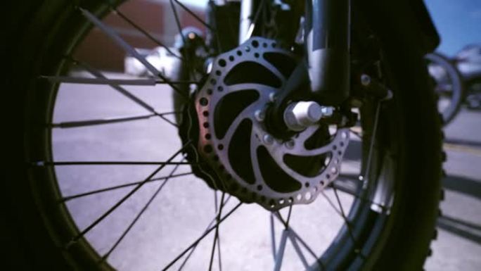 从模糊到锋利的车轮和电动机的电动自行车视图从下面显示。电动自行车电机摄像机运动滑动特写。停车场有自然