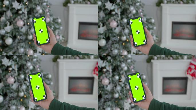 男子在新年装饰的房间里拿着模拟智能手机绿屏铬钥匙。在发光的圣诞家居室内，男性手握黑色现代智能手机的特