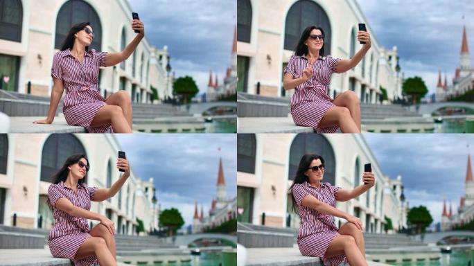 可爱的女士微笑着自拍，在欧洲城市使用智能手机。4k龙红相机