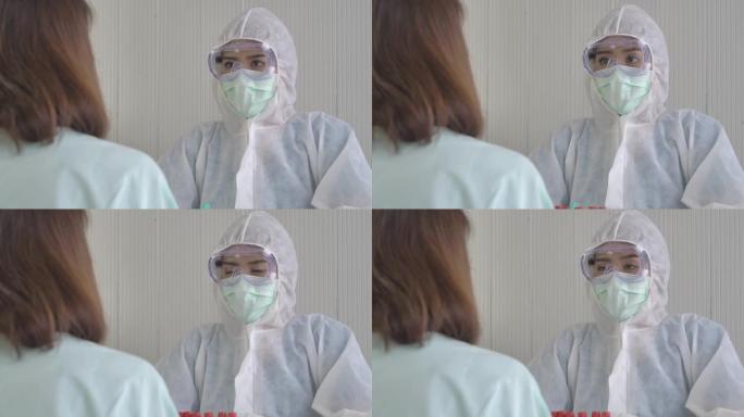 穿着PPE套装 (个人防护用品套装) 的女医生戴着医用口罩与一名女患者交谈。