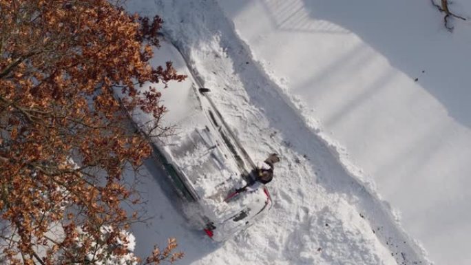 一名成年男子在冬季暴风雪后从雪地上清洗汽车。加速无人机视频正上方鸟瞰。