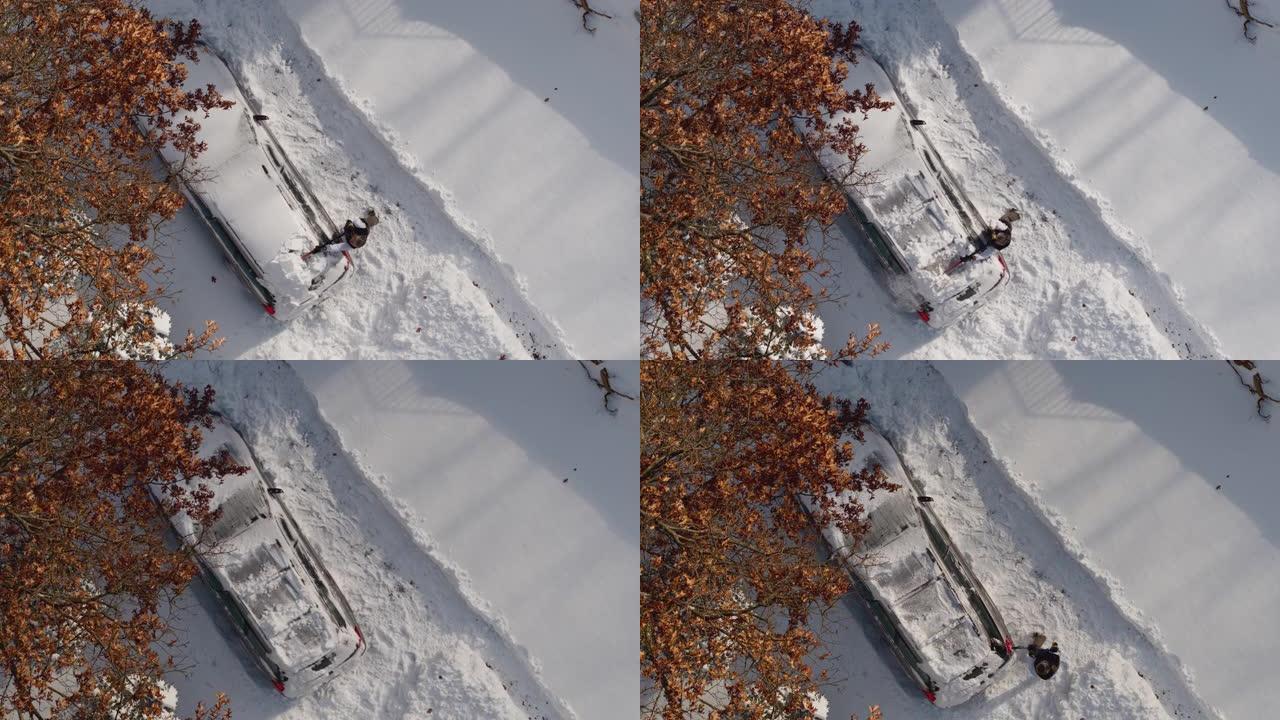 一名成年男子在冬季暴风雪后从雪地上清洗汽车。加速无人机视频正上方鸟瞰。