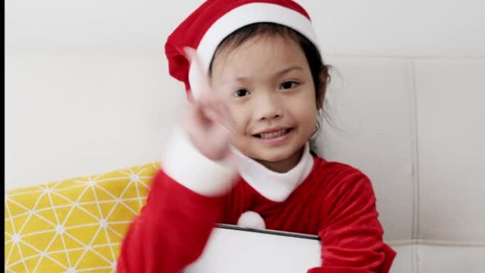 快乐的亚洲女孩穿着圣诞老人服装，在家坐在沙发上，生活理念。