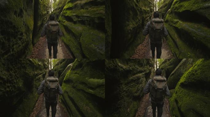 一个人正穿过峡谷。他背着一个大背包。岩石周围布满了苔藓。从后面射击。在山里徒步旅行。4K DCI