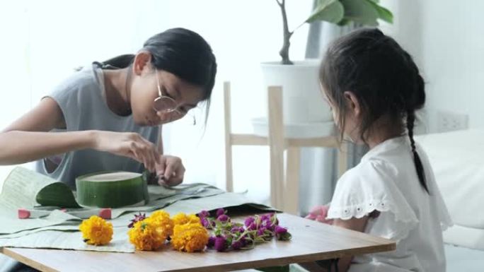 快乐的亚洲孩子在家里一起制作kathong (用香蕉叶和花朵制成，漂浮在河中祈祷和感谢)，为晚上做准