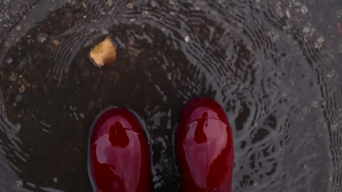 穿着橡胶红色防水靴的女人在寒冷的天气里穿过秋天的泥坑