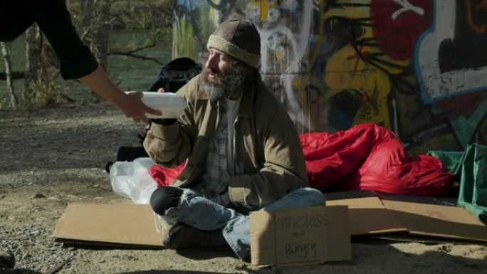 一个女人把一盒可以带走的食物送给一个饥饿的无家可归的人