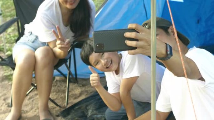 快乐的亚洲家庭父母和孩子用您的手机拍照，度假时要去露营。