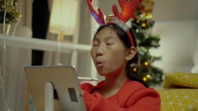 快乐的亚洲女孩穿着红色毛衣，在家里用圣诞装饰品在数字平板电脑上唱歌和绘画，生活方式概念。