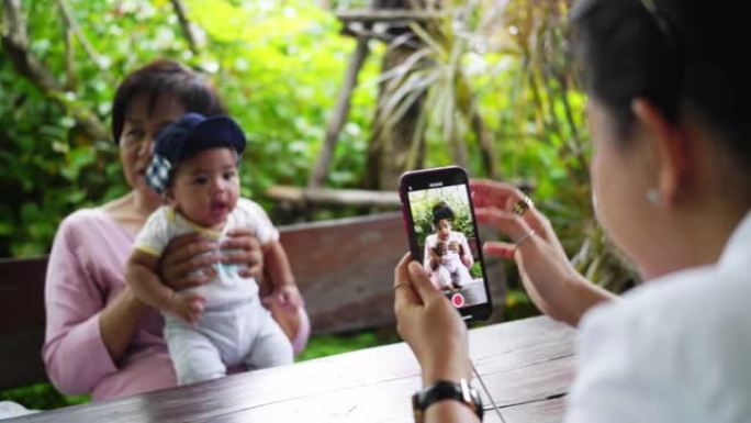 一位亚洲母亲正在家里的花园里拍祖母抱着男婴的照片