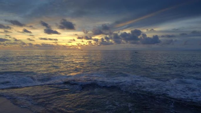 在美丽的日落期间，热带海滩上的高潮波浪，深蓝色海洋中的船只剪影