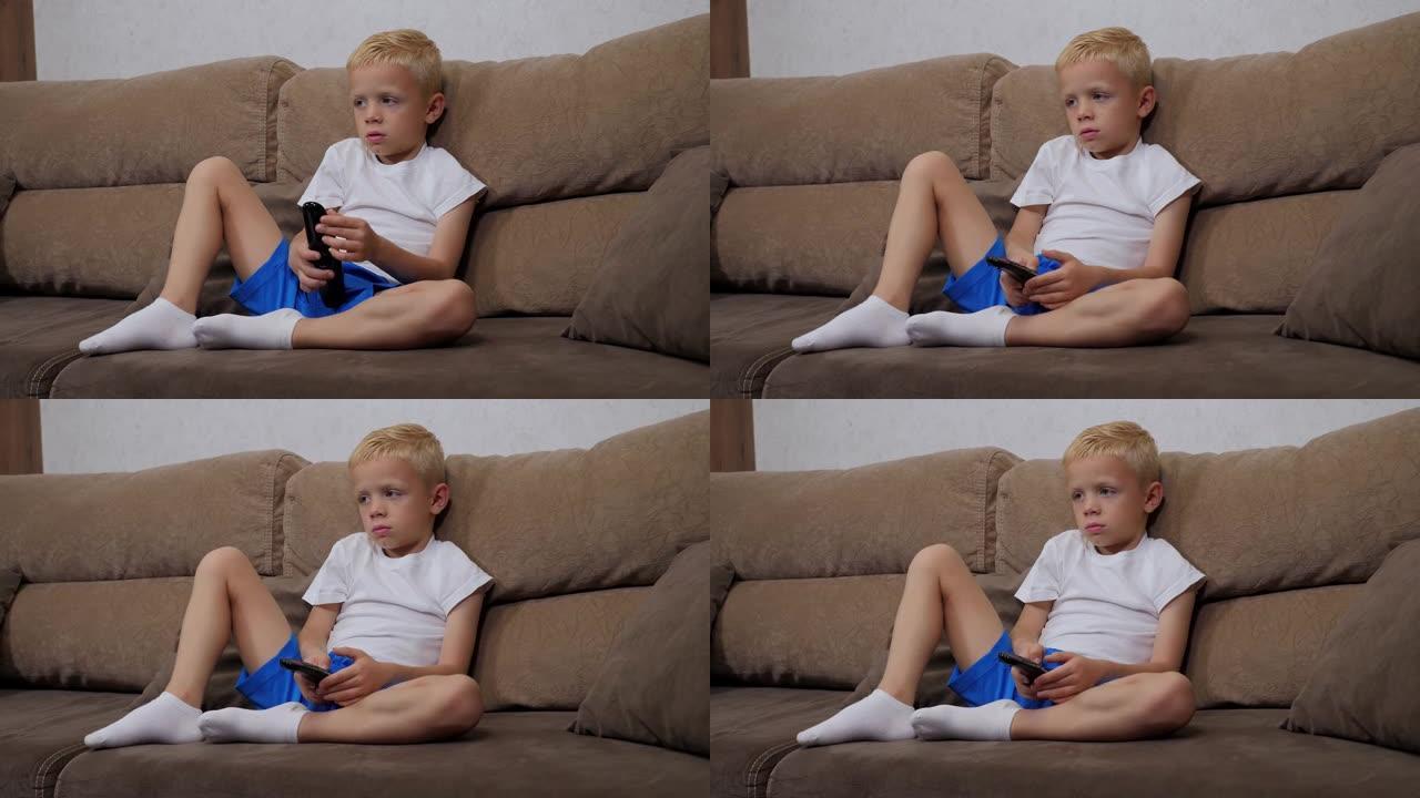 悲伤的小男孩坐在家里的沙发上，在电视上切换频道